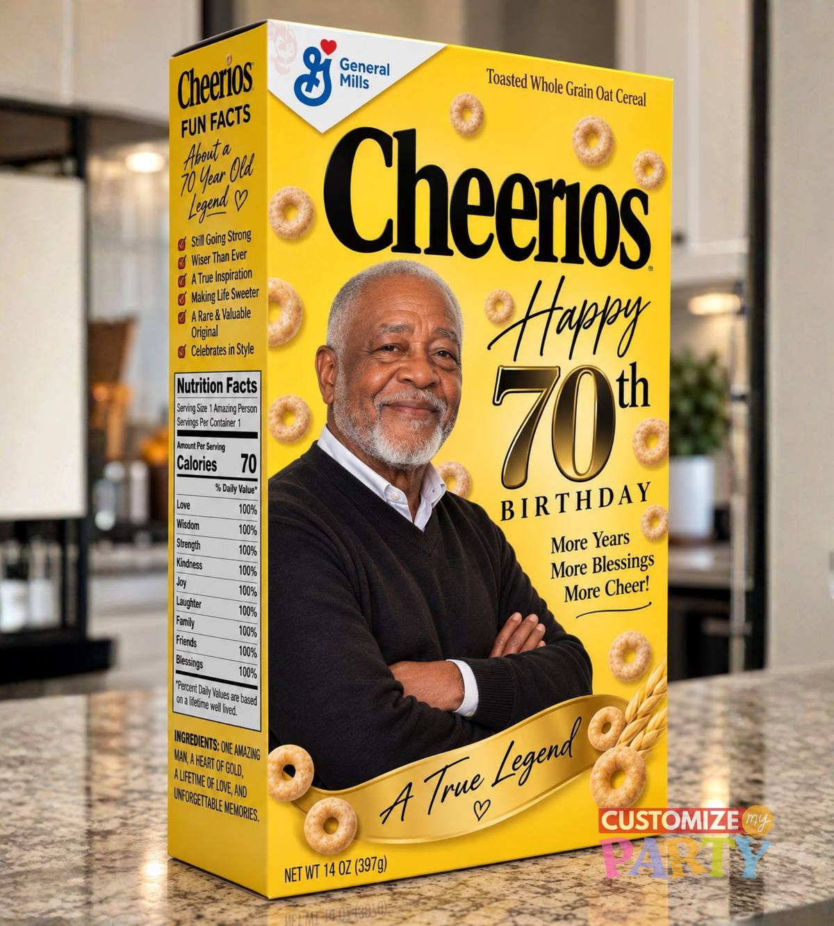 A yellow General Mills Cheerios cereal box with a 70th birthday theme, featuring a photo of a smiling man and illustrations of Cheerios. The box is shown standing on a kitchen countertop with a blurred kitchen background.