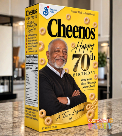 A yellow General Mills Cheerios cereal box with a 70th birthday theme, featuring a photo of a smiling man and illustrations of Cheerios. The box is shown standing on a kitchen countertop with a blurred kitchen background.
